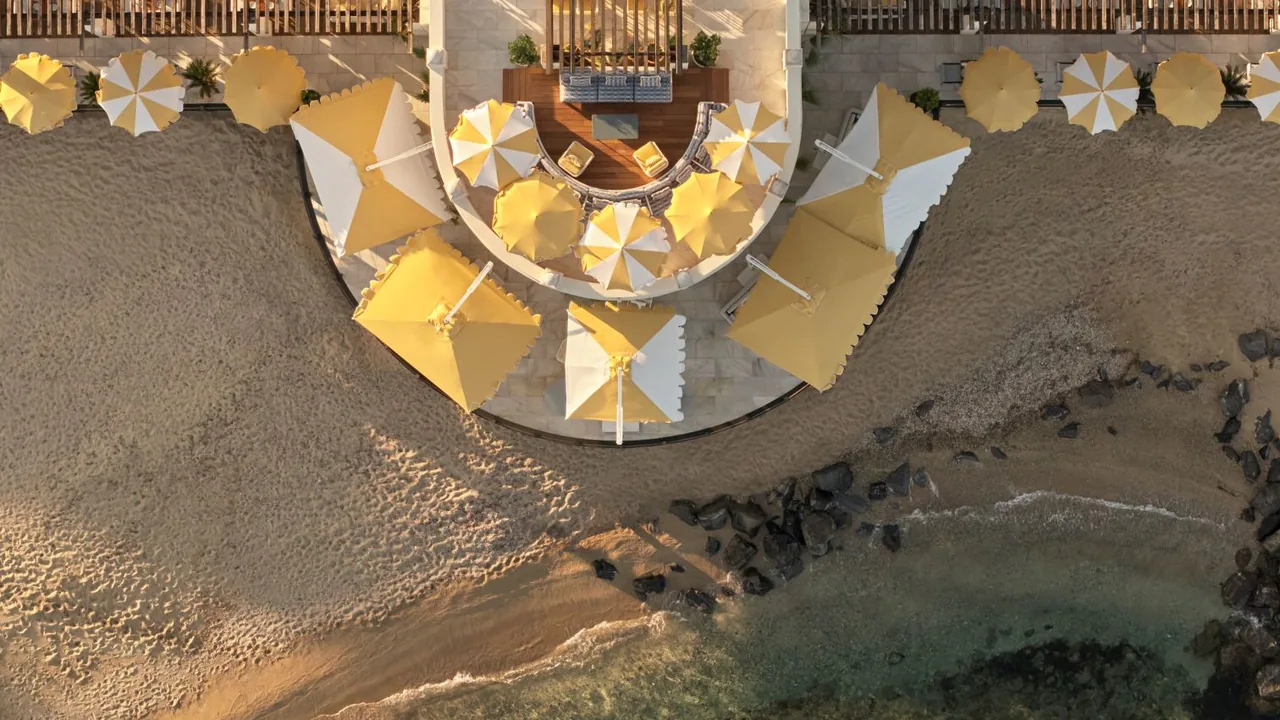 Vue aérienne du beach club du domaine : sable, parasols dorés et eau turquoise.